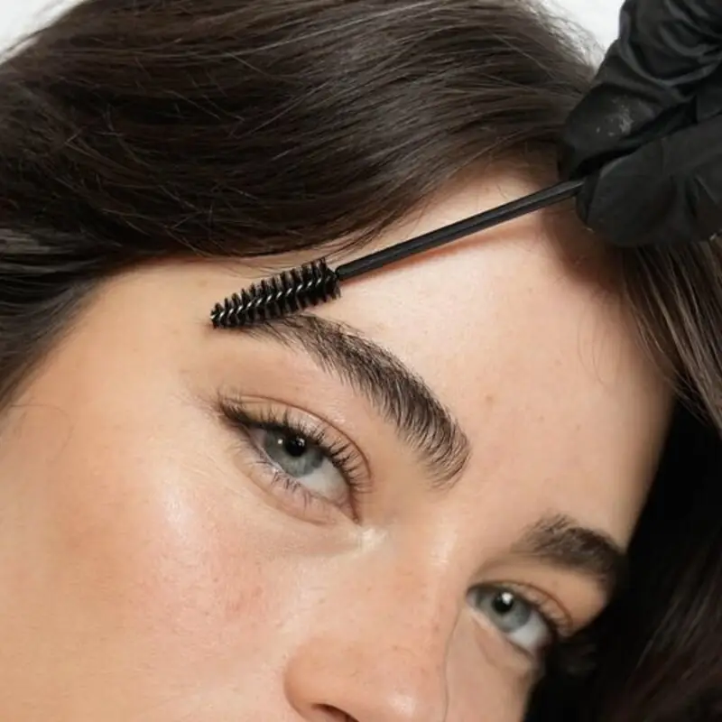 Detalhe da escovinha penteando os fios da sobrancelha no efeito brushed brow